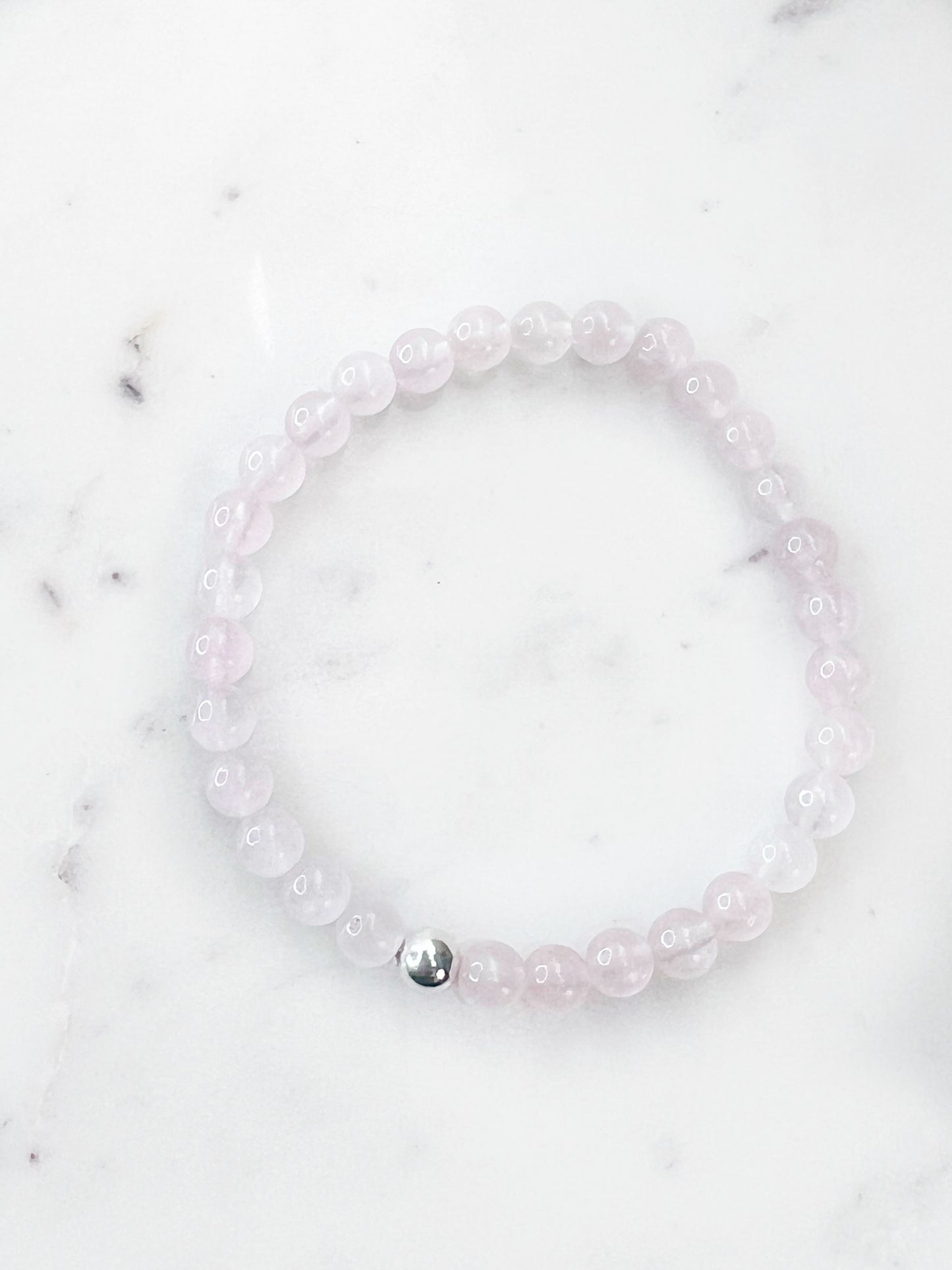 Rose Quartz stretch bracelet with one silver bead on a marbled white background.