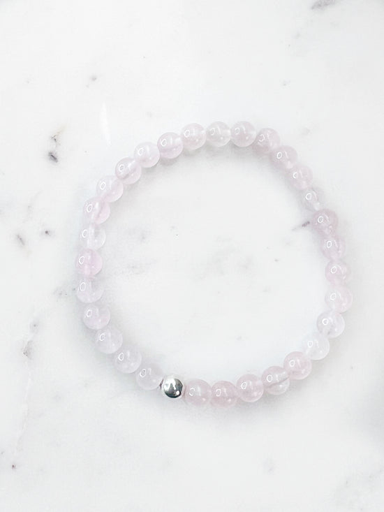 Rose Quartz stretch bracelet with one silver bead on a marbled white background.