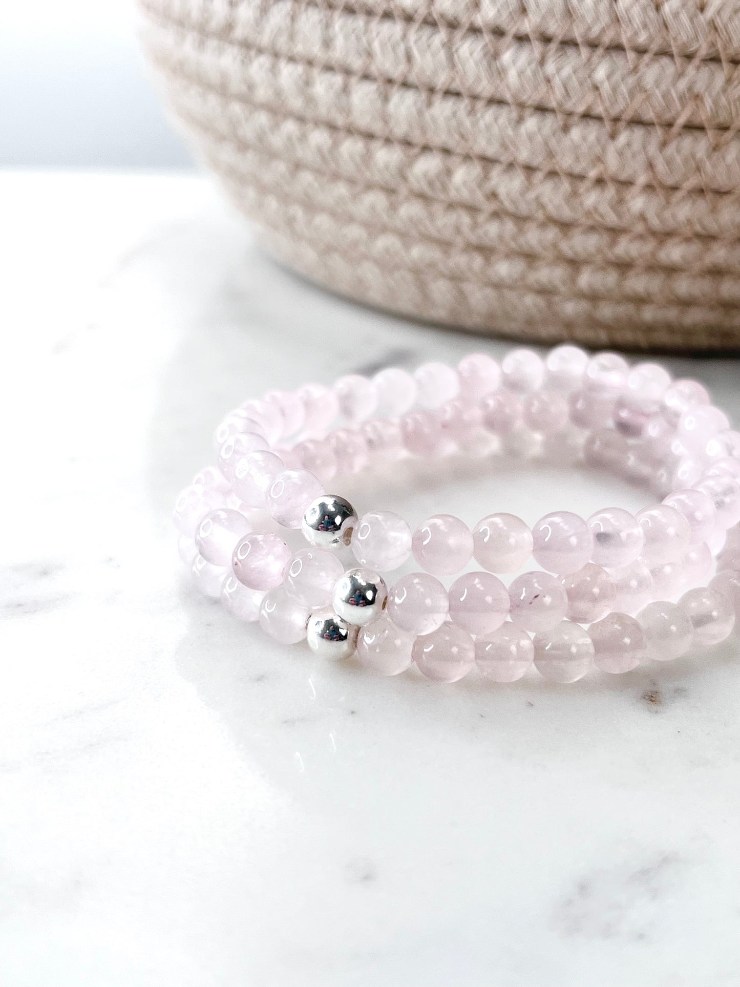 three light pink rose quartz stretch bracelets with one silver bead on each. in front of a brown woven basket