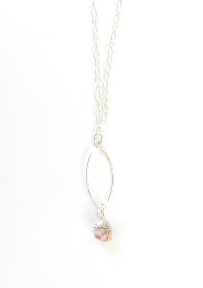 A Sterling Silver necklace with a flat long oval pendant with a pink tourmaline nugget hanging from the bottom. It's on a white background.