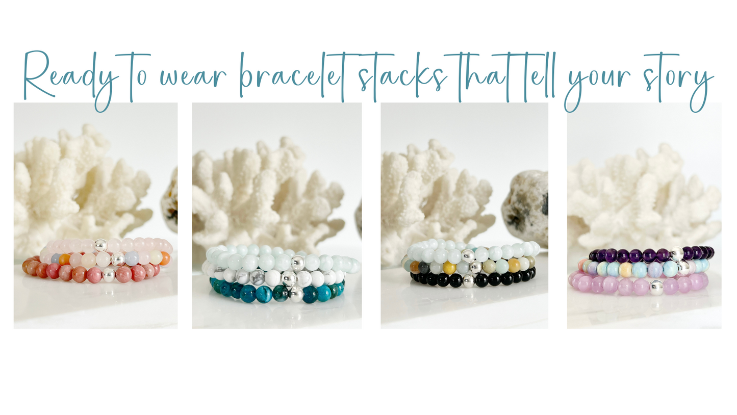 four sets of 3 gemstone stretch bracelets each. each one is all the same gemstone and has one silver bead each. there are white coral and a brown rock behind the stacks.