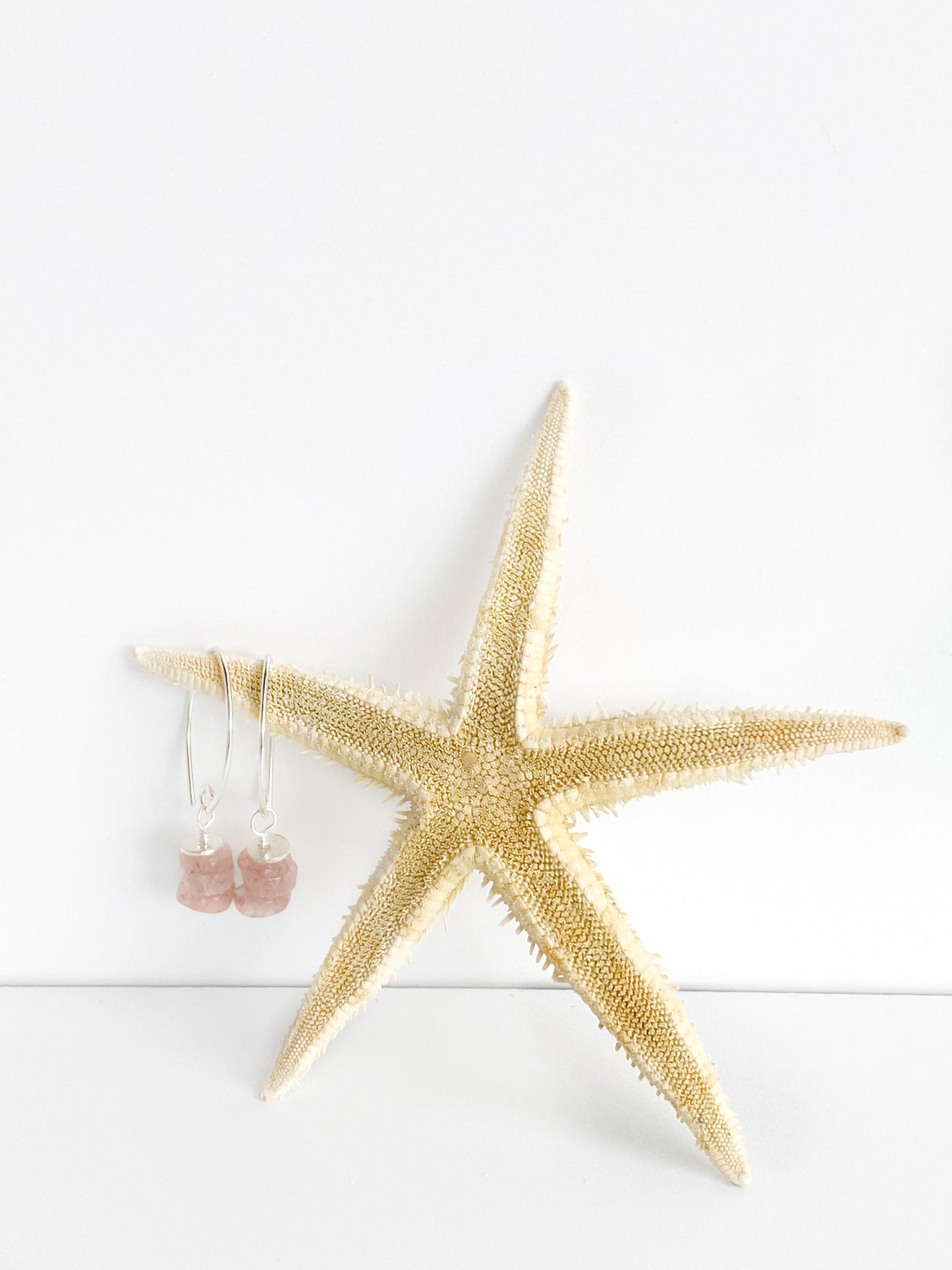 handmade strawberry quartz and sterling earrings hung on a point of a starfish