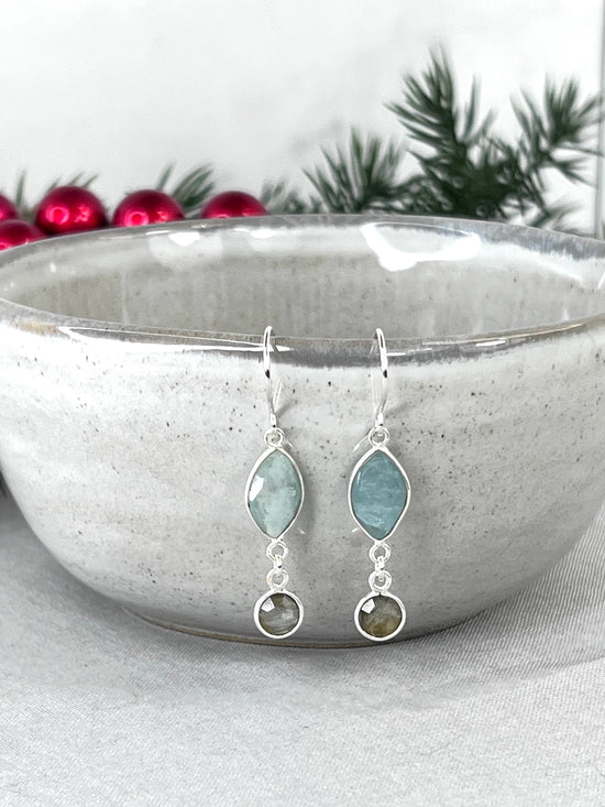 Handmade sterling ear wires with aquamarine marquis shaped drops with small labradorite circles at the bottom. Hanging from a grey ceramic small bowl with fake xmas props