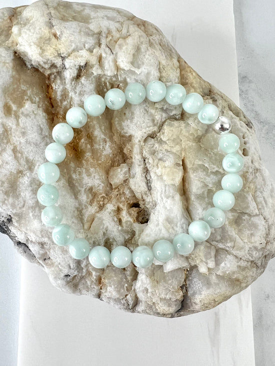 Casual everyday Green Moonstone stretch bracelet with one Sterling Silver bead on a brownish rock.