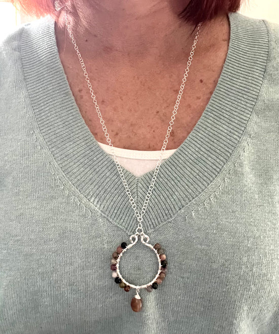 A woman wearing a sage green v neck sweater with a small part of a white tank top underneath. She's wearing a long Sterling Silver round necklace with small Tourmaline beads wire wrapped around it with a teardrop Tourmaline bead hanging from the bottom.