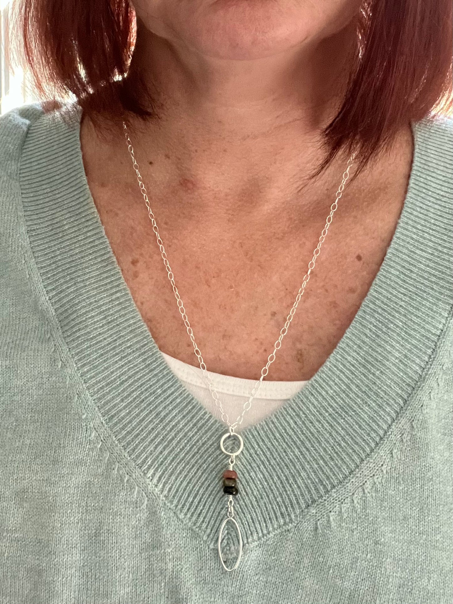Woman wearing a sage green sweater with a white tank top and a Sterling silver necklace with three Tourmaline rondelles and a flat silver oval at the bottom