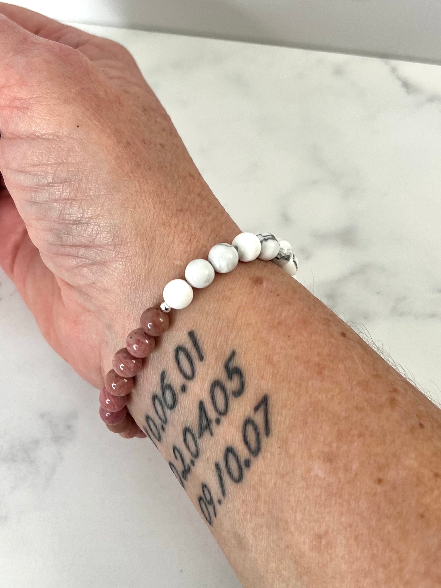 a woman's arm with three number tattoos and a howlite and rhodonite stretch bracelet on.