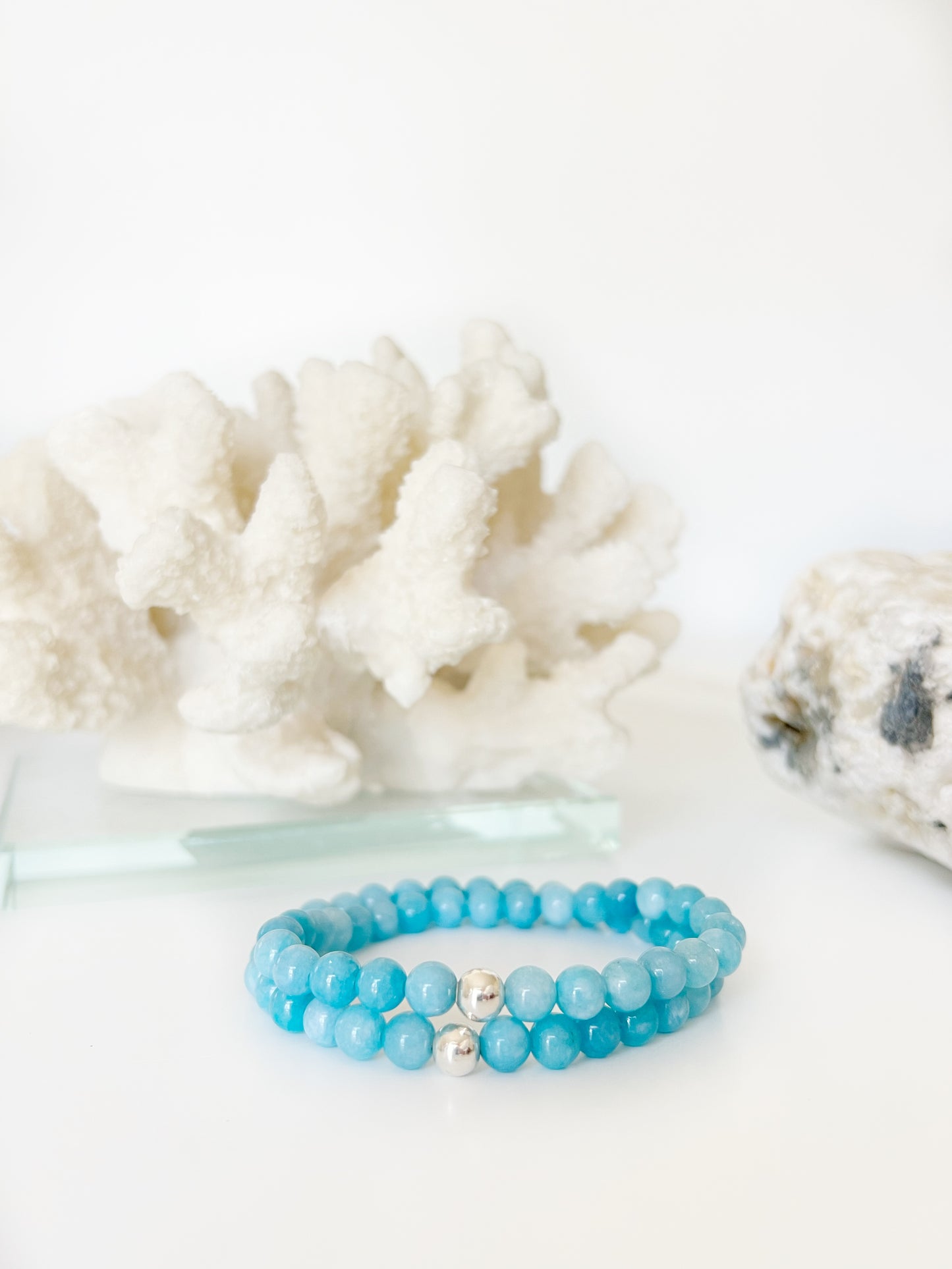 Set_of_two_Blue_Chalcedony_stretch_bracelets_with_one_Sterling_Silver_bead in front of white coral and a brownish rock