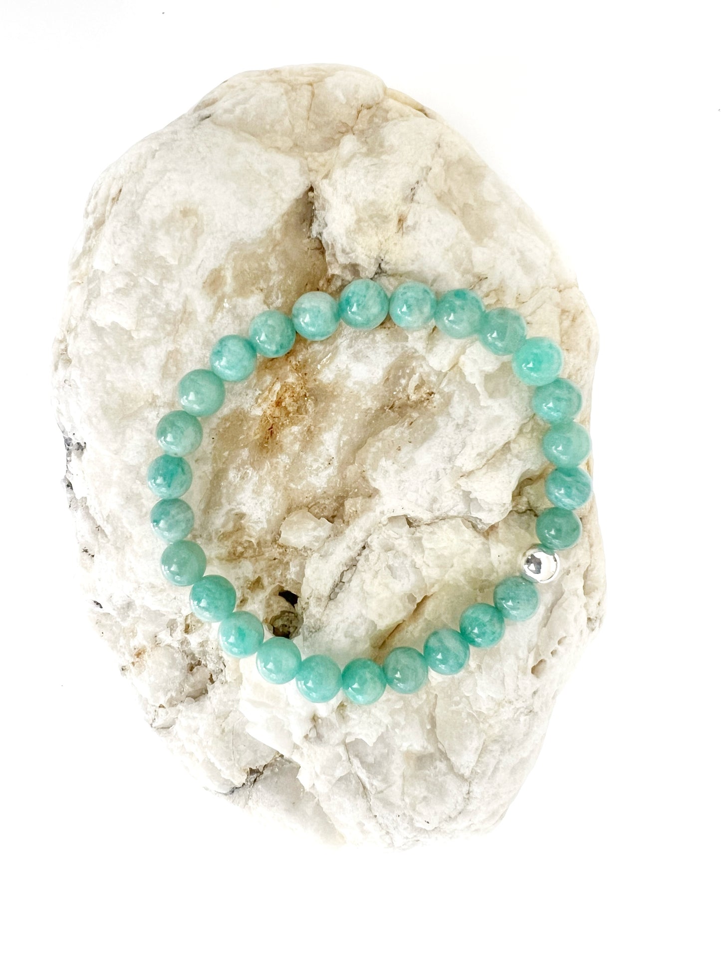 Simple Amazonite stretch bracelet with one Sterling Silver bead on a brownish rock with a white background