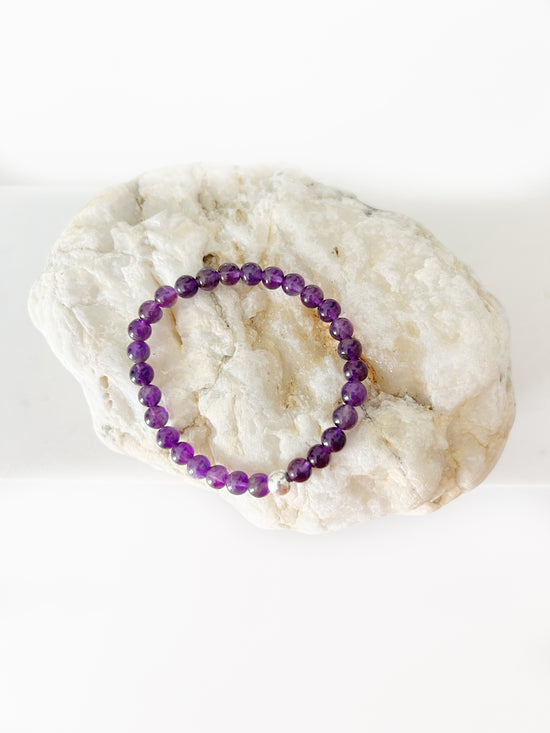 amethyst stretch bracelet with one silver bead on a whitish colored rock