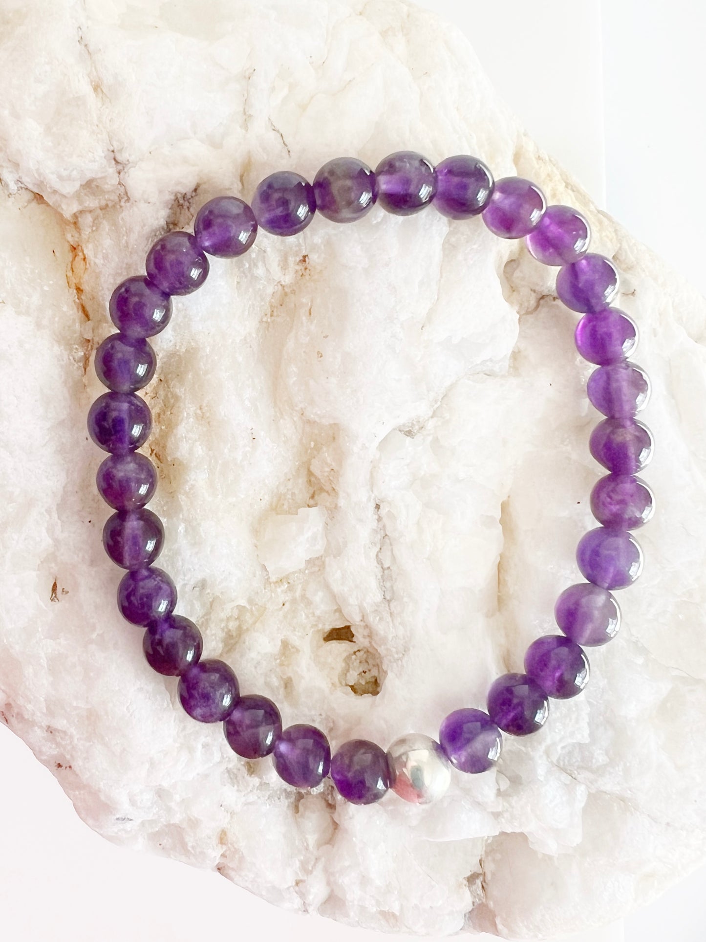 amethyst stretch bracelet with one silver bead on top of brownish and white rock.