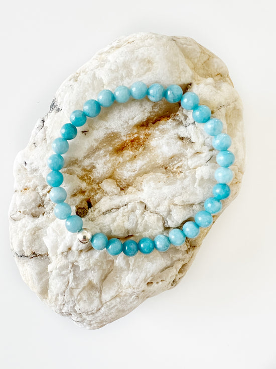 Simple everyday Blue Chalcedony stretch bracelet with one Sterling Silver bead on it on top of brown and white rock.
