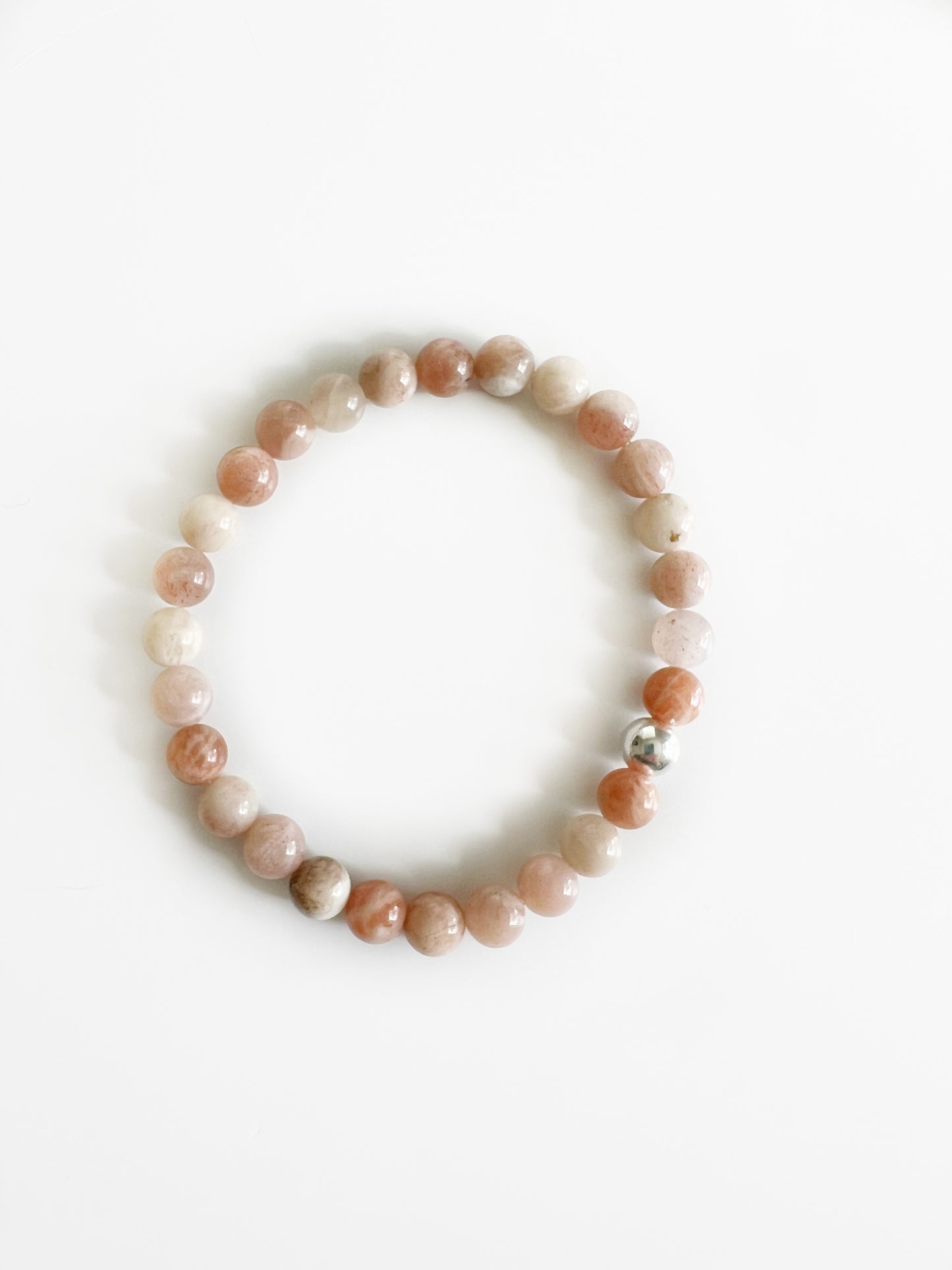 peach moonstone stretch bracelet with one silver bead on a white background