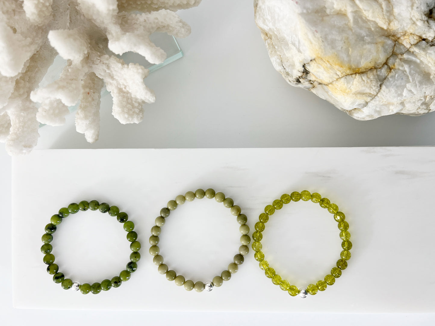 Three different stretch bracelets next to each other on a white background with white coral and a brownish rock behind them.